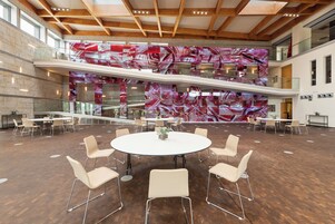 A spacious indoor area with a central round table surrounded by chairs, multiple levels with glass railings, and a large abstract mural on the back wall.