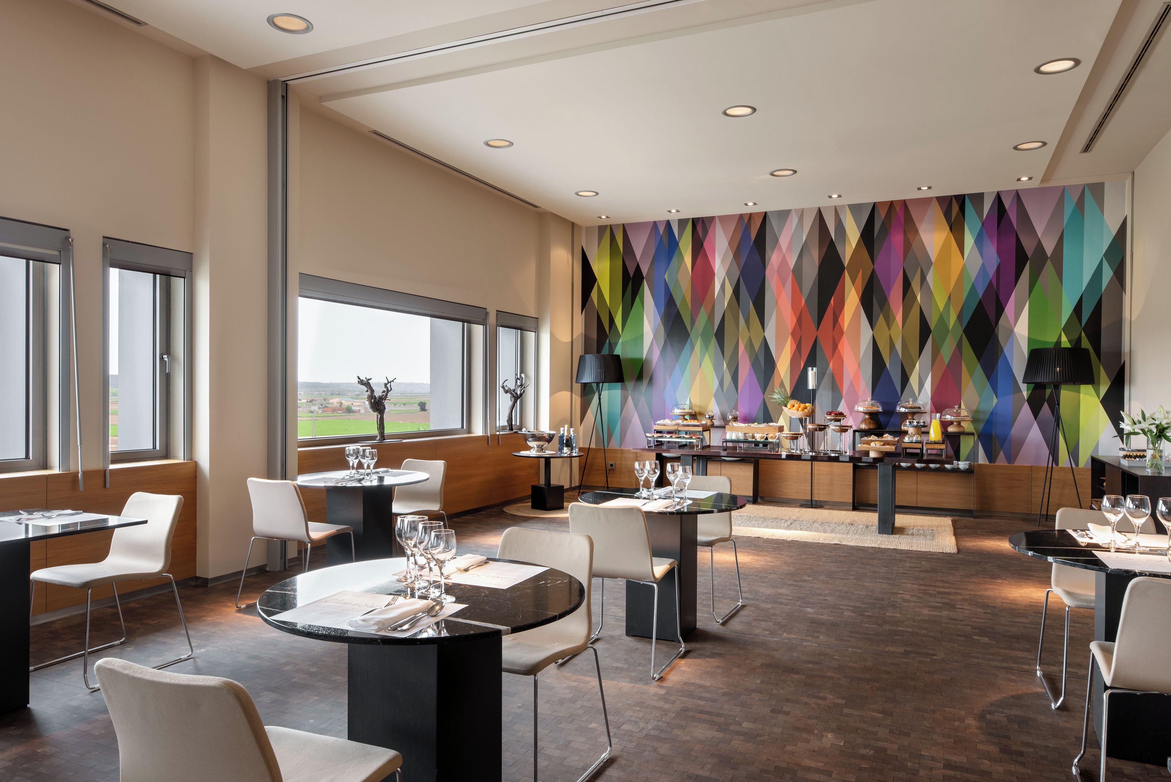 A modern dining area with round tables, white chairs, and a colorful geometric wall.