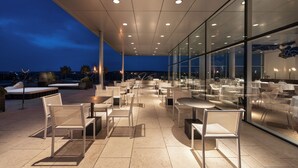 An outdoor dining area with modern furniture and glass walls, providing views of the cityscape at dusk. - Valbusenda Hotel Bodega and Spa (Toro)