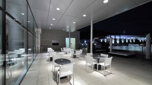 A modern outdoor dining area with glass walls, white furniture, and a view of the city at night. - Valbusenda Hotel Bodega and Spa (Toro)