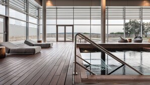 A modern indoor pool area with wooden flooring, lounge chairs, and large windows offering views of the outdoors. - Valbusenda Hotel Bodega and Spa (Toro)