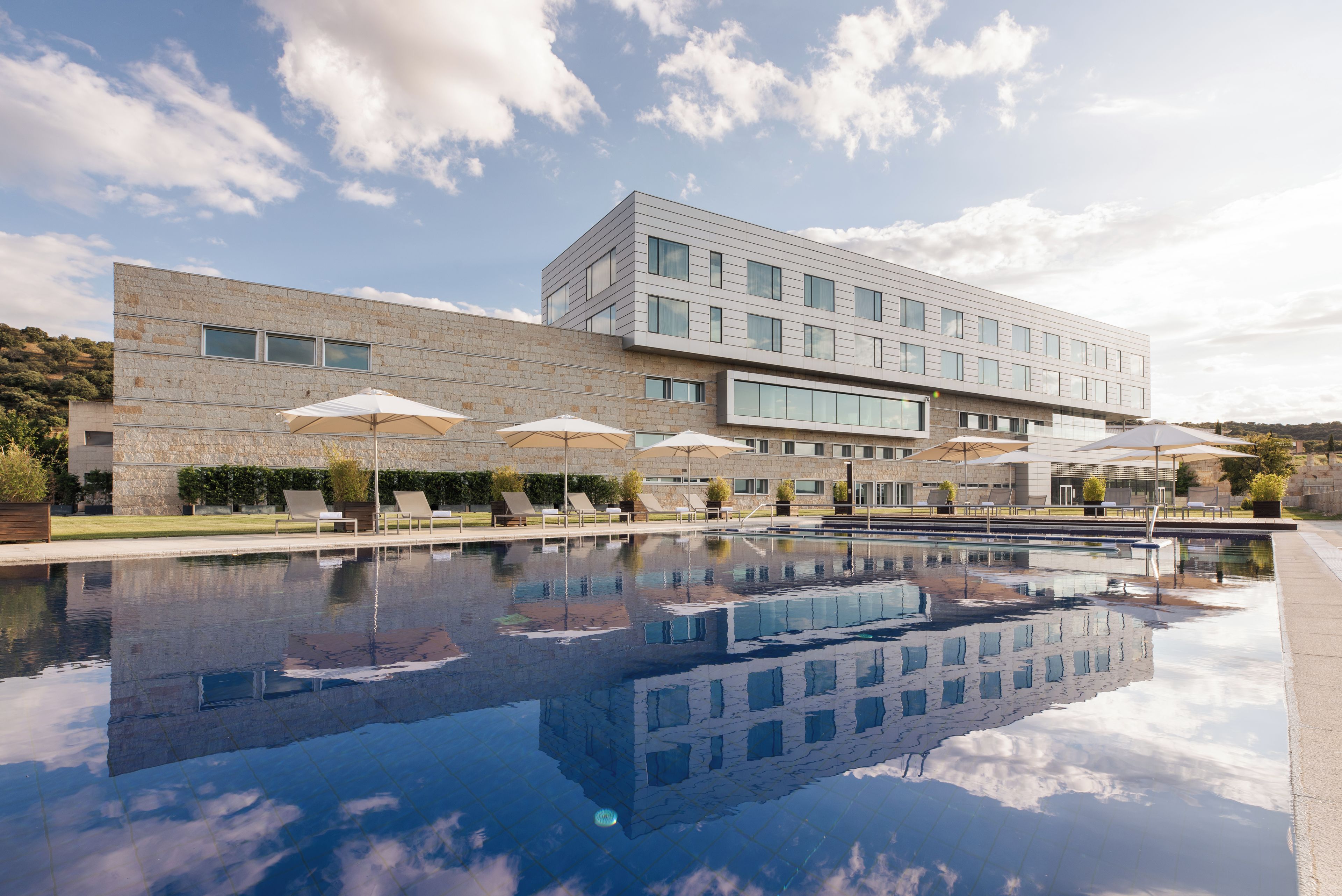 Un edificio moderno con piscina, asientos exteriores y sombrillas.