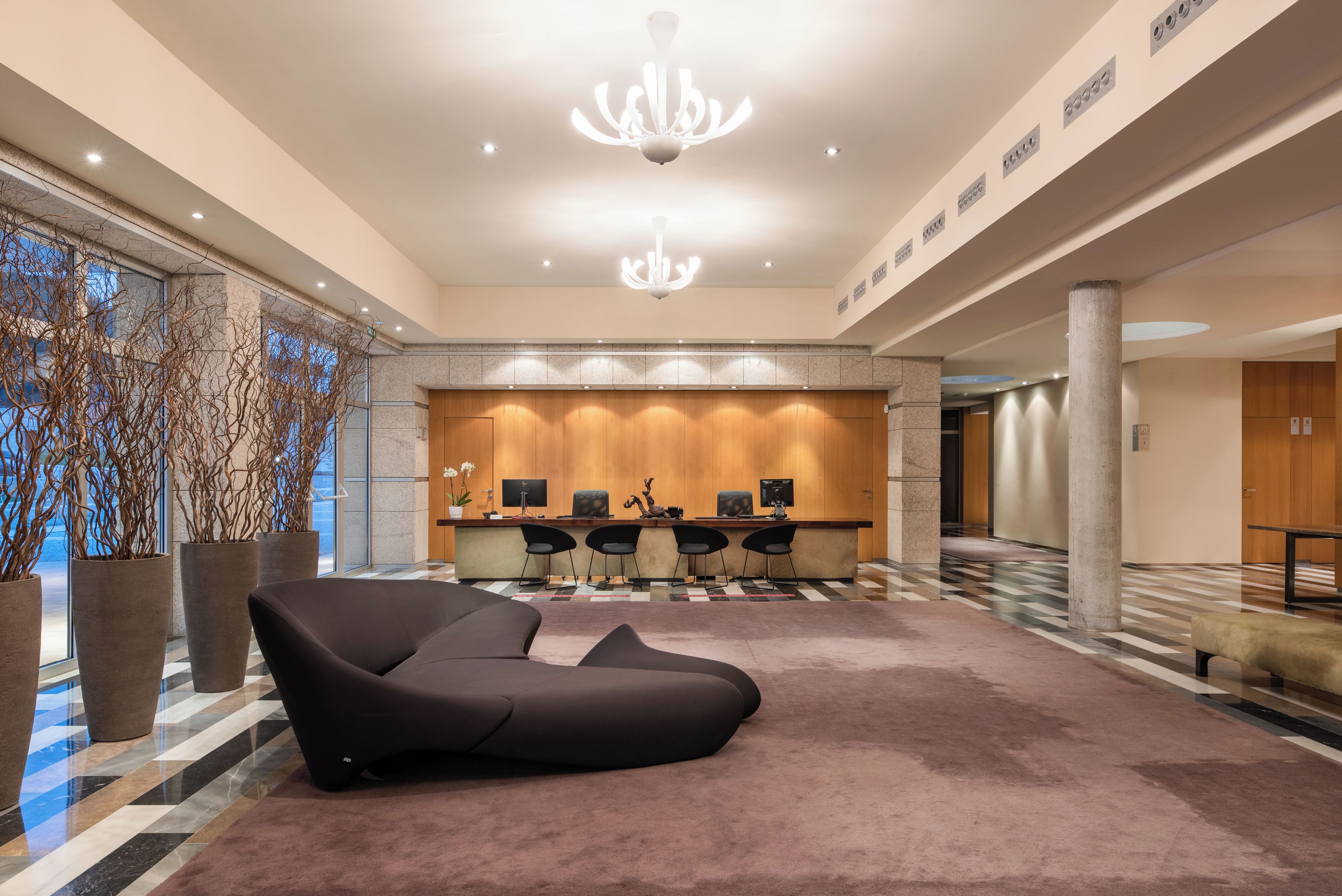 A modern lobby with a reception desk, seating area, and large windows.