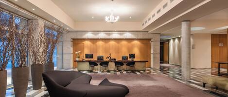 A modern lobby with a reception desk, seating area, and large windows.