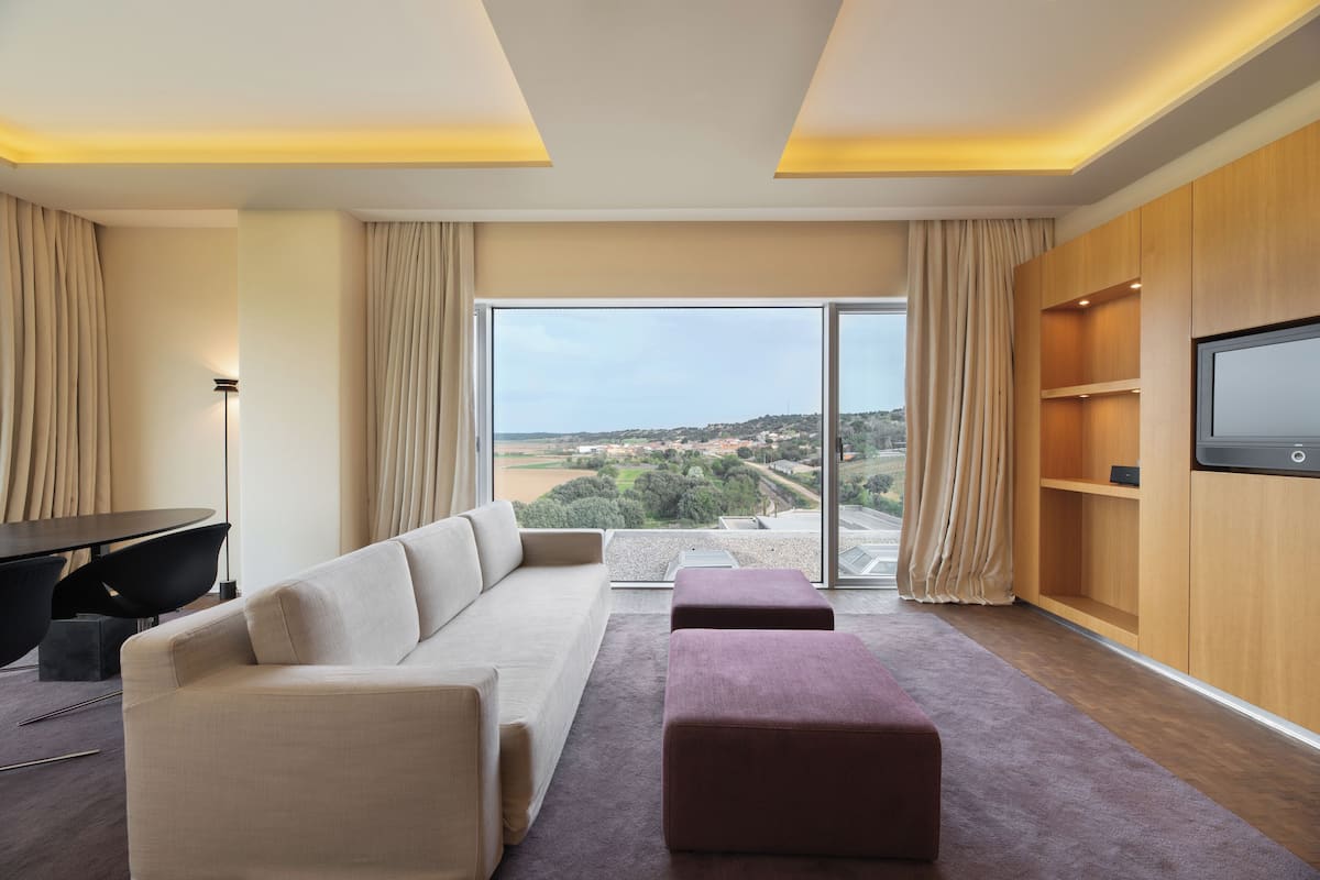 A modern living room with a sofa, ottoman, and a TV on a wooden wall.
