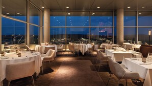 A restaurant with round tables and chairs, large windows, and a view of the city at night. - Valbusenda Hotel Bodega and Spa (Toro)