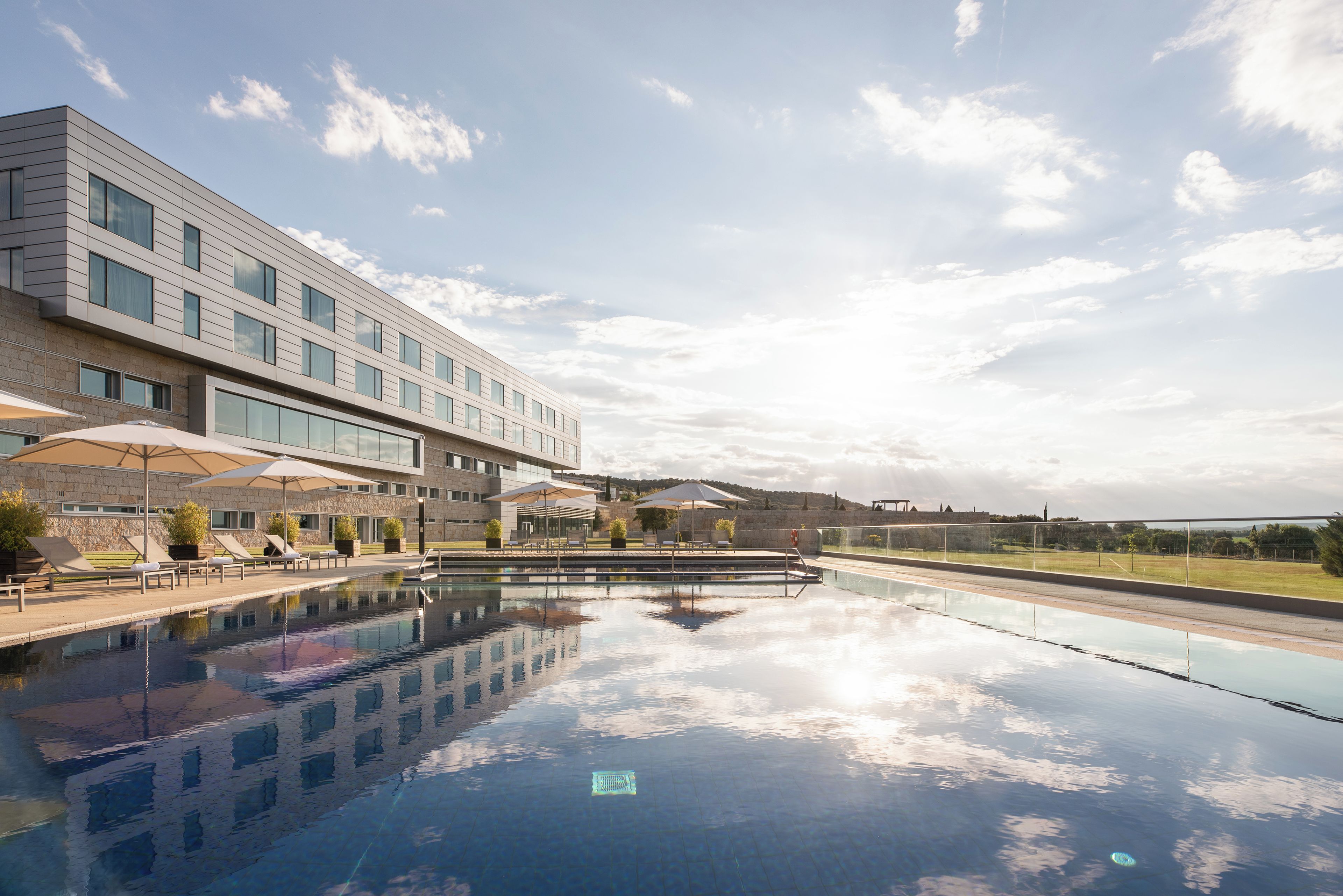 Un edificio moderno con piscina, mobiliario exterior y sombrillas.