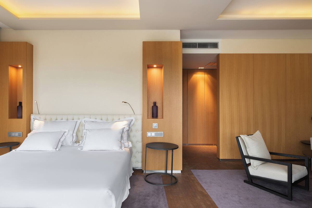 A modern hotel room with a large bed, a small round table, a chair, and a wooden wardrobe.