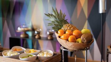 Un frutero sobre una mesa con diversas frutas y una vela al fondo.