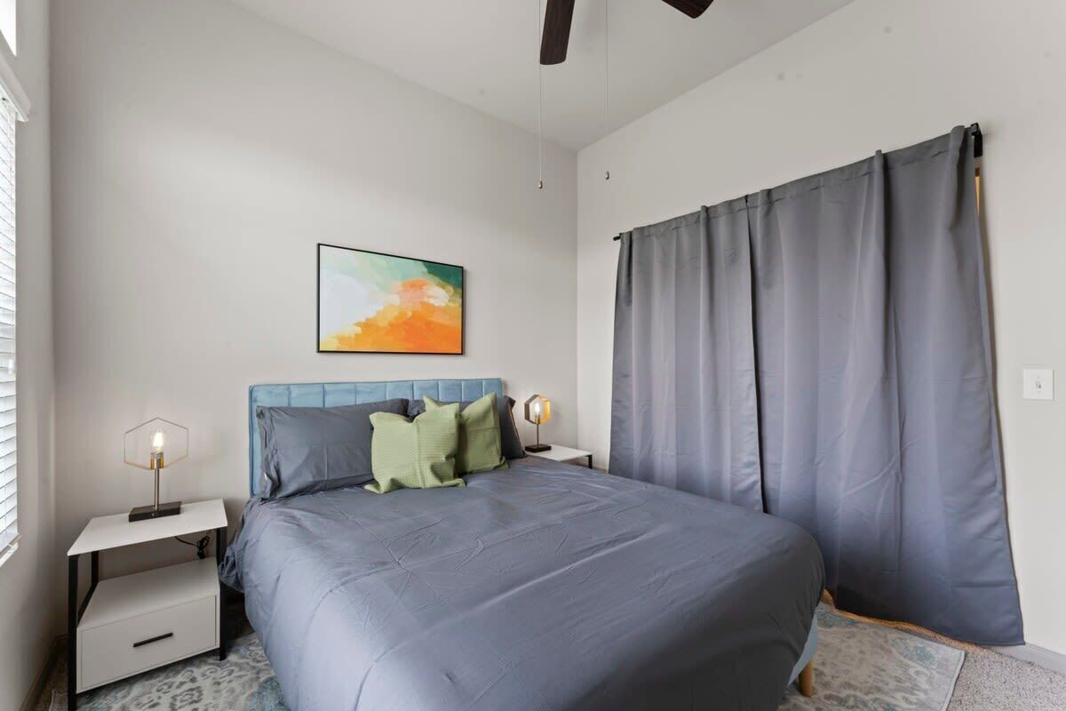 A bedroom with a bed, nightstands, a wall-mounted artwork, and a window with curtains.