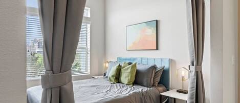 A bedroom with a bed, a bedside table, a lamp, and a window with curtains.