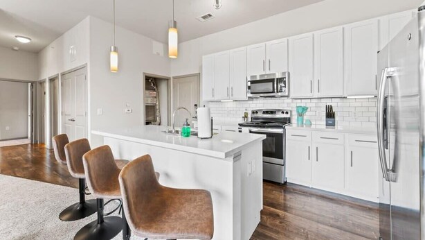 Una cocina moderna con armarios blancos, electrodomésticos de acero inoxidable y una isla central con taburetes de bar.