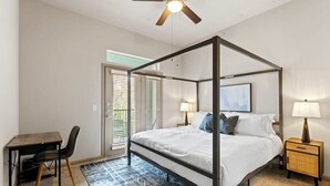Una cama con dosel, un ventilador de techo, un escritorio con silla y una mesita de noche con lámpara.