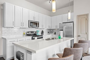 A modern kitchen with white cabinets, stainless steel appliances, and a central island with bar stools.