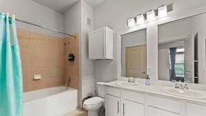 Un baño moderno con bañera, dos lavamanos, inodoro y un espejo grande.