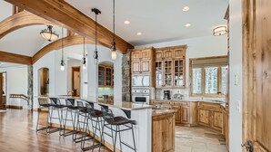 A spacious kitchen with wooden cabinets, a large island with bar stools, and a stone accent wall. - Free SkyCard Act-Lux Ski & Golf Villa, Hot Tub, Home Theater, Billiards, Wet Bar (Breckenridge)