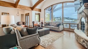 A spacious living room with a fireplace, large windows offering a mountain view, and wooden beams on the ceiling. - Free SkyCard Act-Lux Ski & Golf Villa, Hot Tub, Home Theater, Billiards, Wet Bar (Breckenridge)