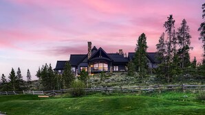A large, dark-colored house with a prominent balcony, surrounded by trees and a grassy area. - Free SkyCard Act-Lux Ski & Golf Villa, Hot Tub, Home Theater, Billiards, Wet Bar (Breckenridge)
