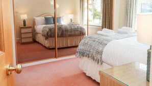 A bedroom with a large mirror, a bed with a white duvet, a bedside table with a lamp, and a window with curtains. - The Old Croft (Buxton)