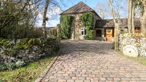 A stone cottage with a cobblestone driveway, ivy-covered walls, and a wooden gate. - The Old Croft (Buxton)