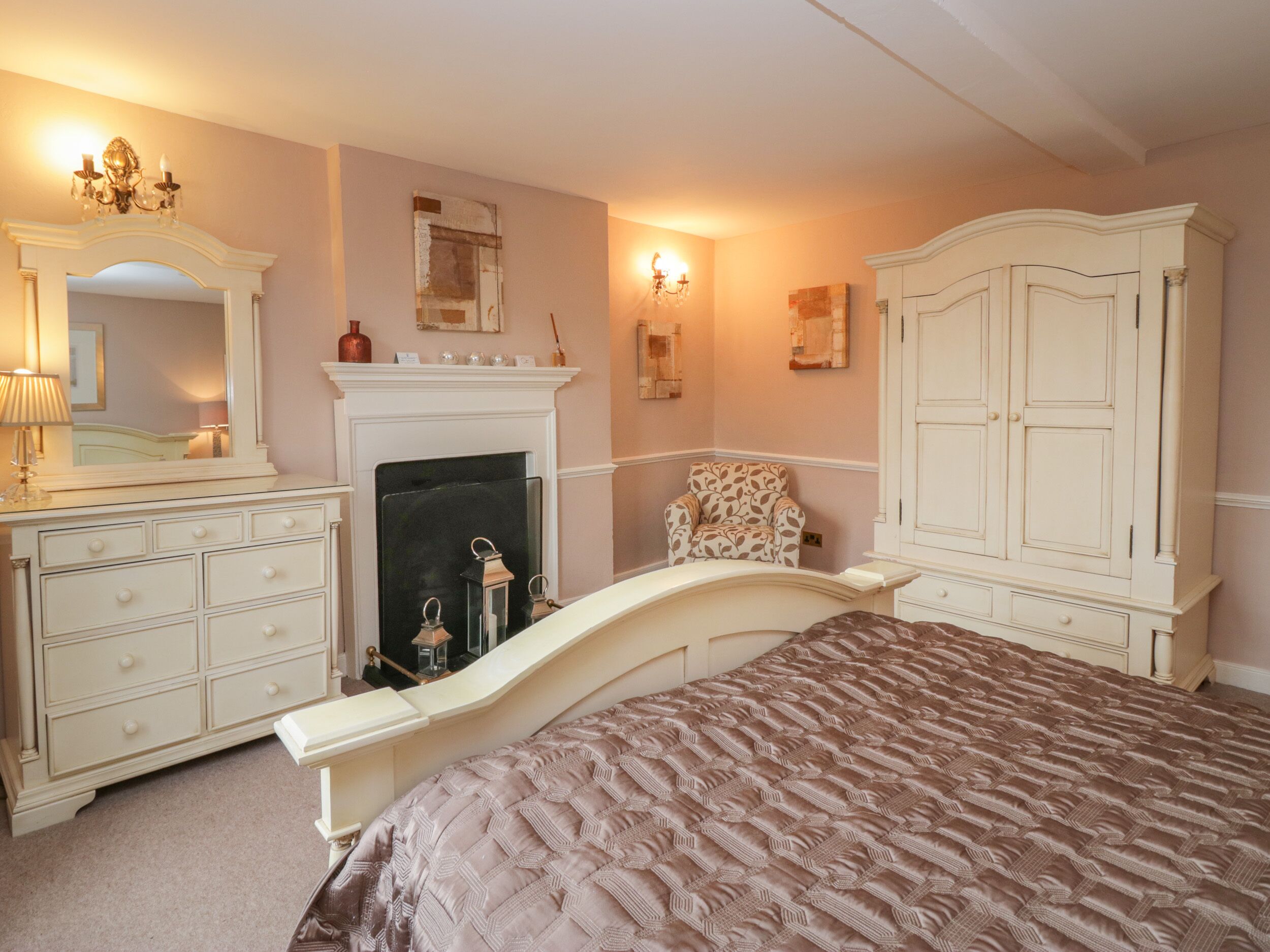Un dormitorio con cama, cómoda, espejo, chimenea y apliques de pared.