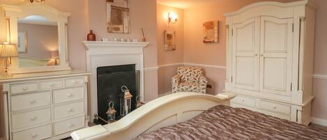 Un dormitorio con cama, cómoda, espejo, chimenea y apliques de pared.