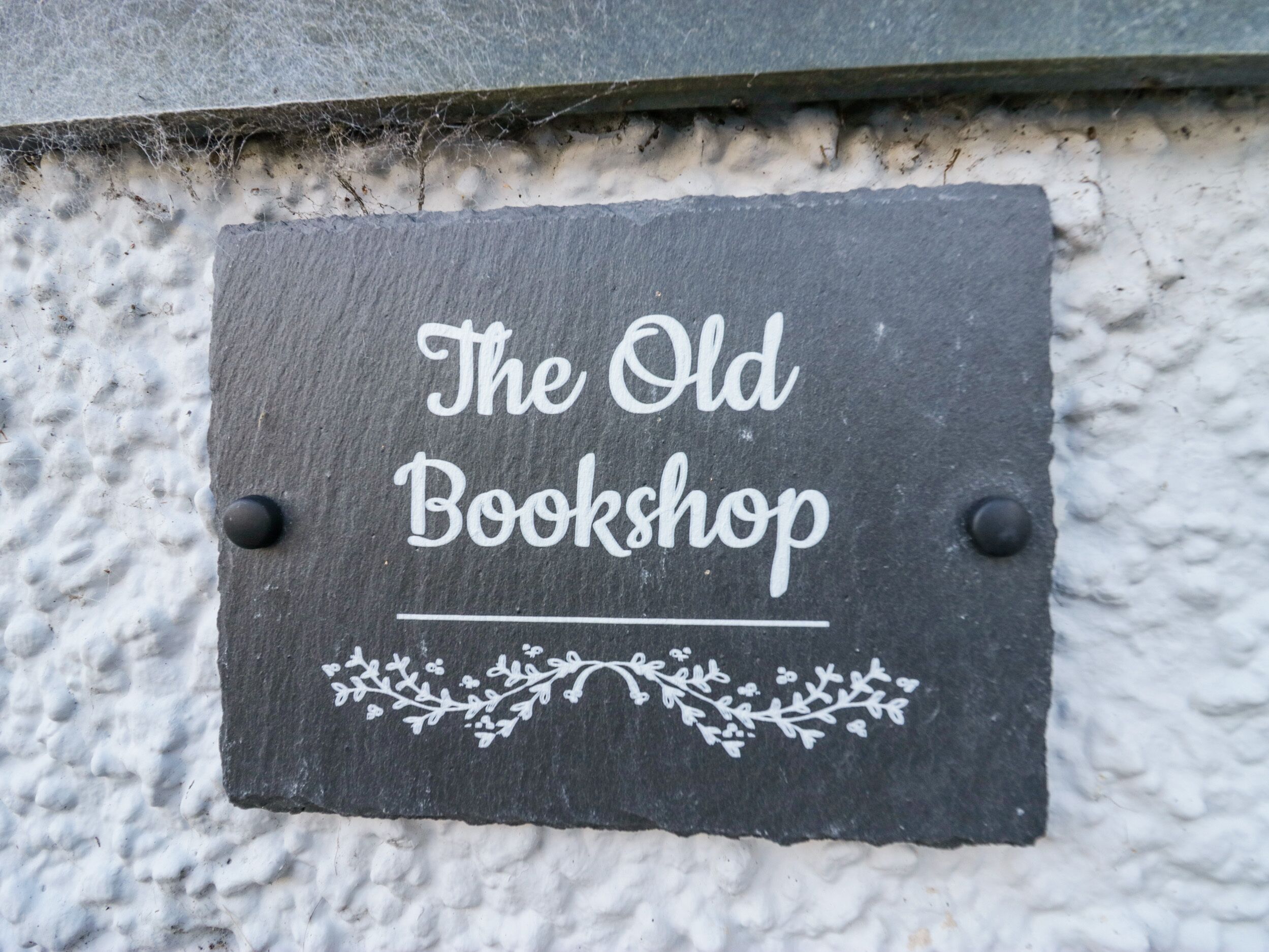 A slate sign with "The Old Bookshop" written on it, mounted on a textured wall.