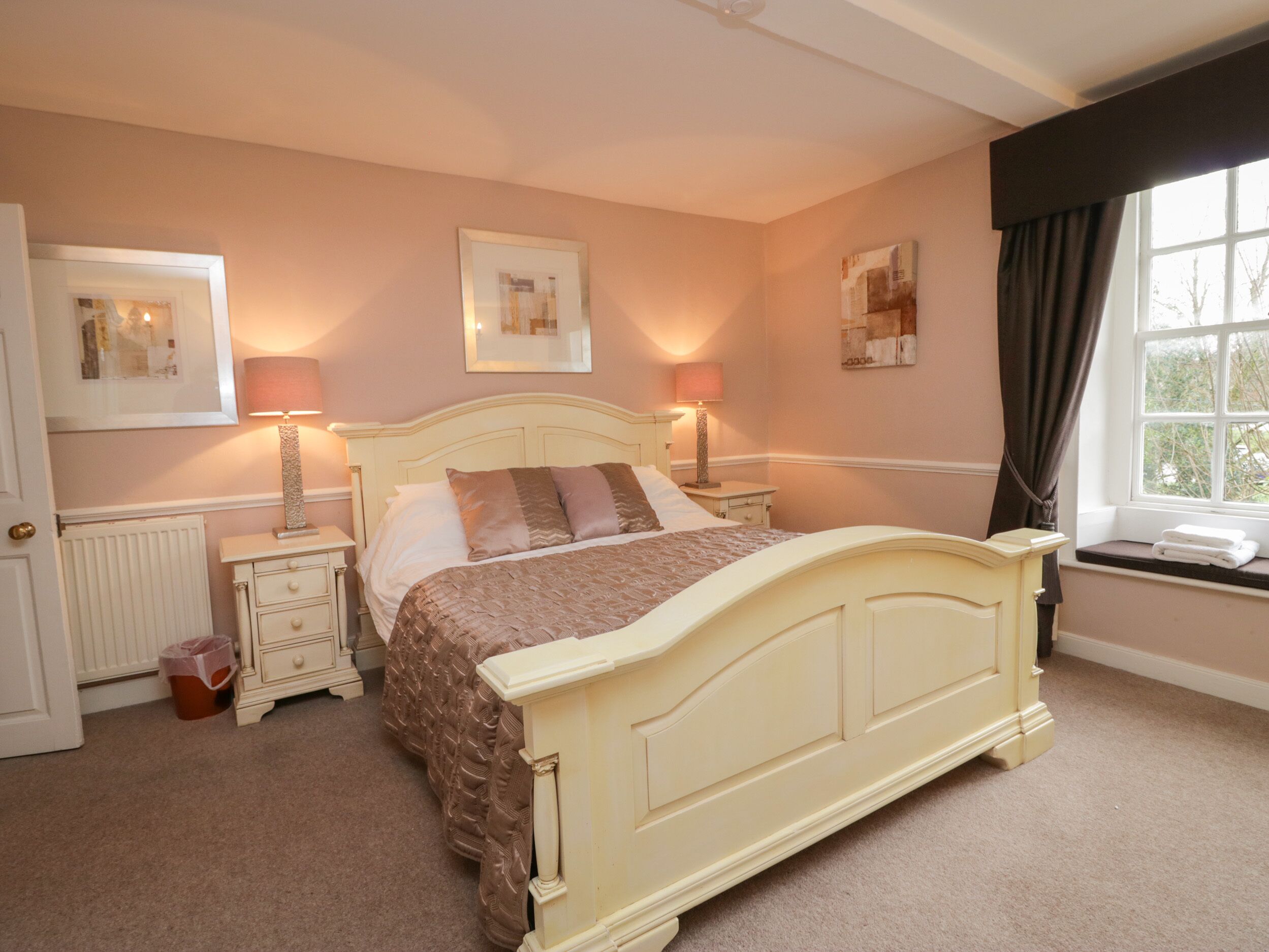 A bedroom with a bed, bedside tables, lamps, a radiator, and artwork on the walls.