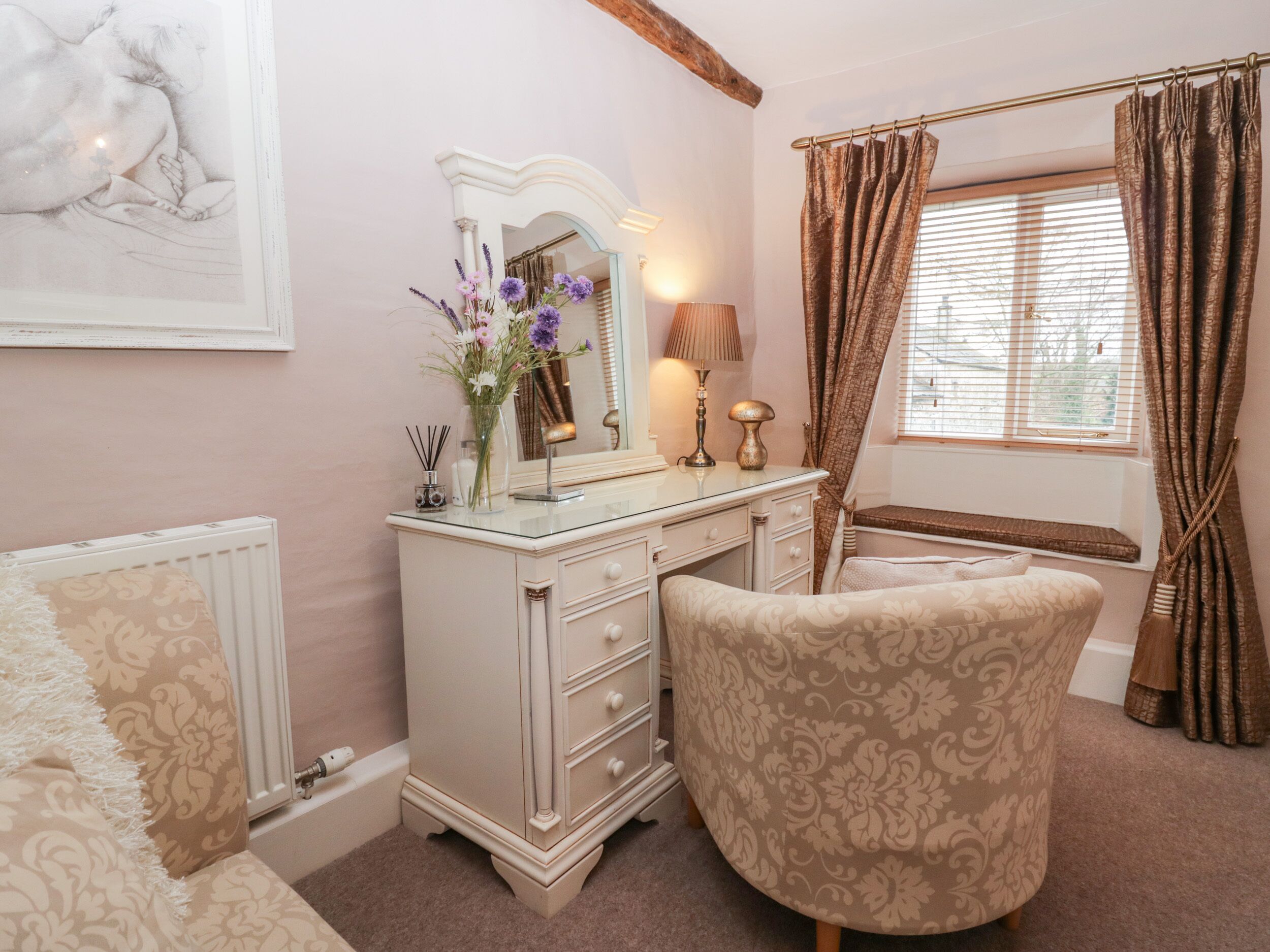 A bedroom with a vanity, a chair, a bed, a window with curtains, and a radiator.