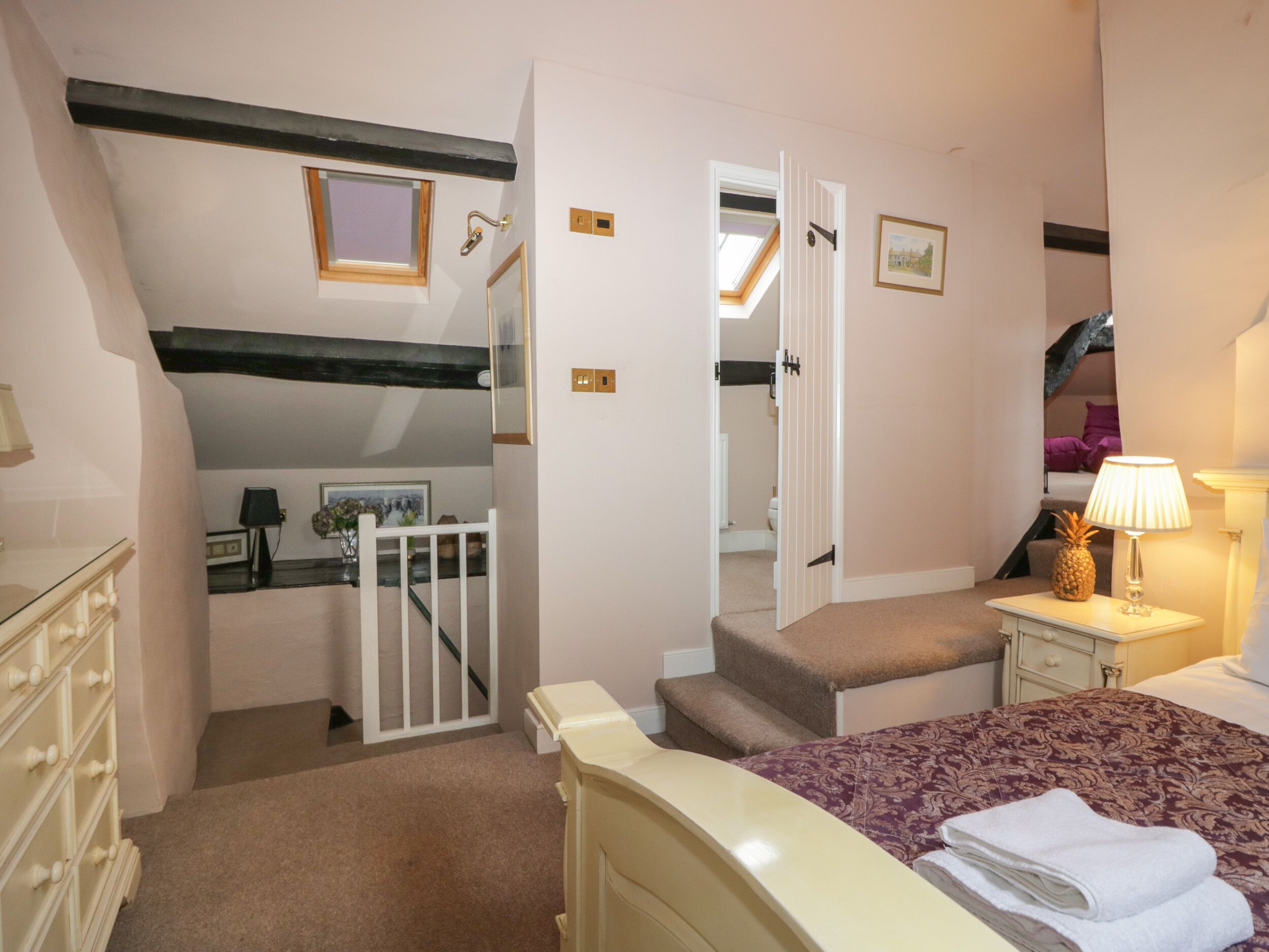 Ein Schlafzimmer mit Bett, Nachttisch, Kommode, Fenster und einer Tür zu einem Badezimmer.