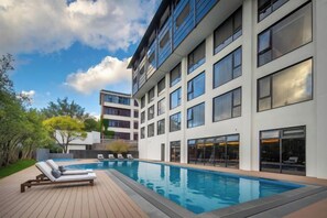 Un hôtel moderne doté d’une piscine, de chaises longues et offrant une vue sur le ciel.