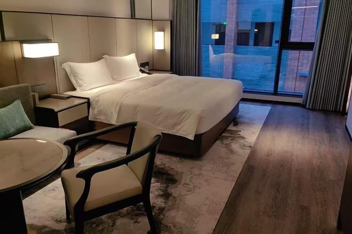 A hotel room with a bed, a desk, a chair, and a view of the outside.
