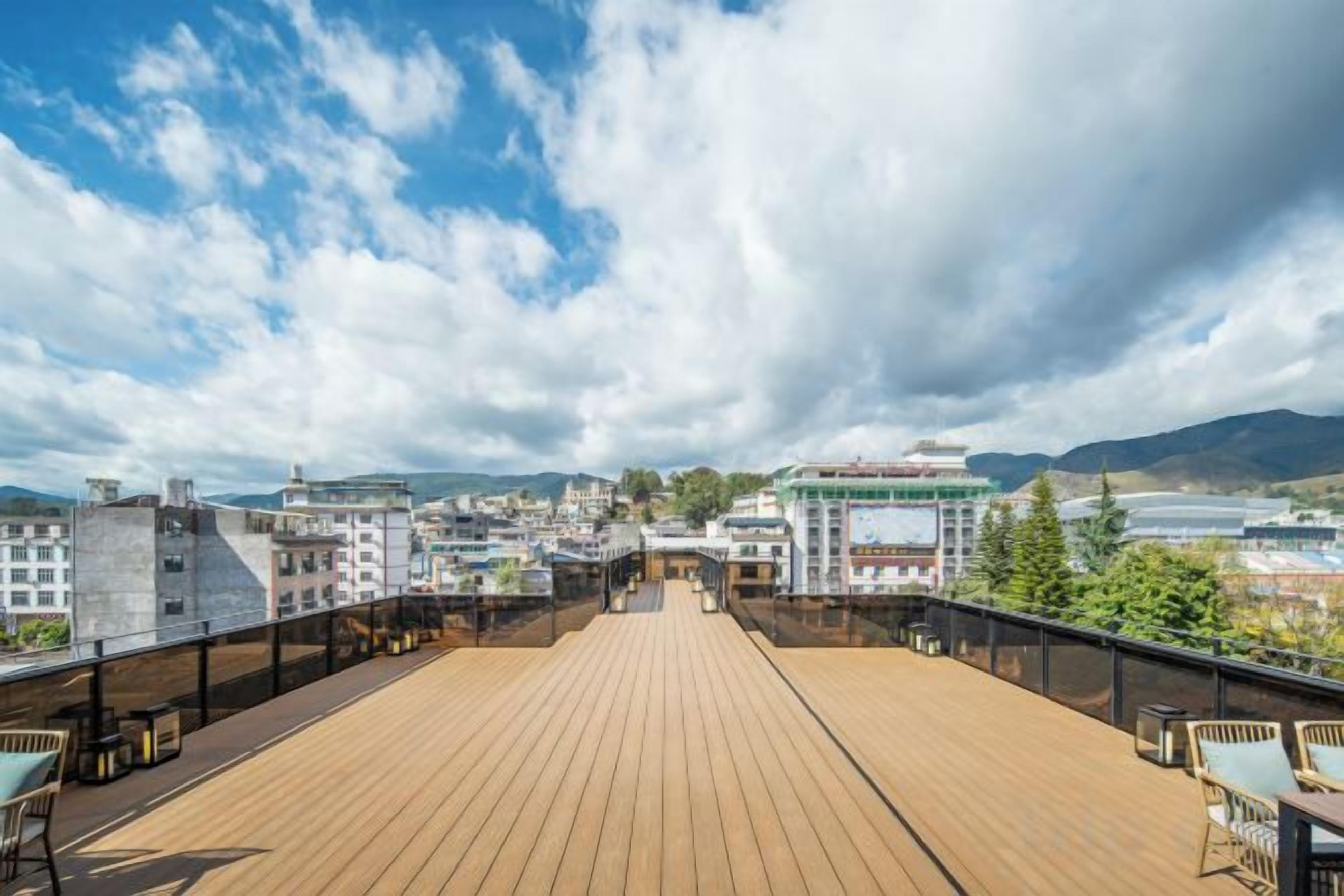 A wooden deck with tables and chairs, overlooking a cityscape with buildings and mountains.