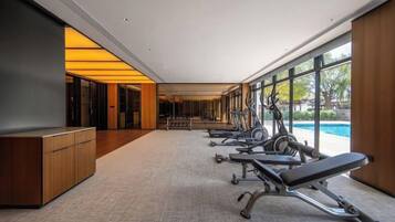 A gym with exercise equipment and a reception desk, large windows, and a view of a swimming pool.