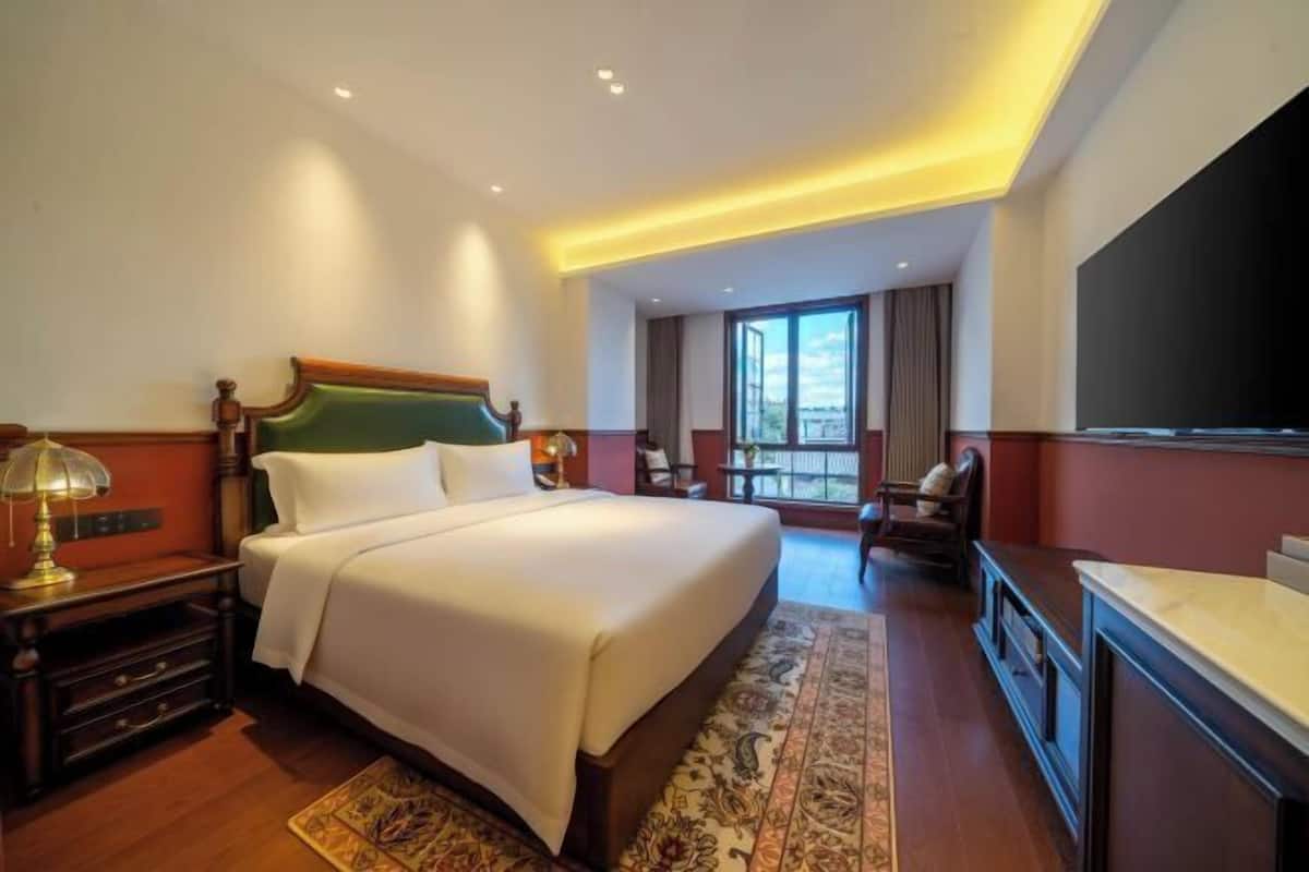 A hotel room with a large bed, a desk, a chair, and a television.