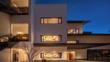 A modern multi-story building with a flat roof, large windows, and a well-lit entrance.