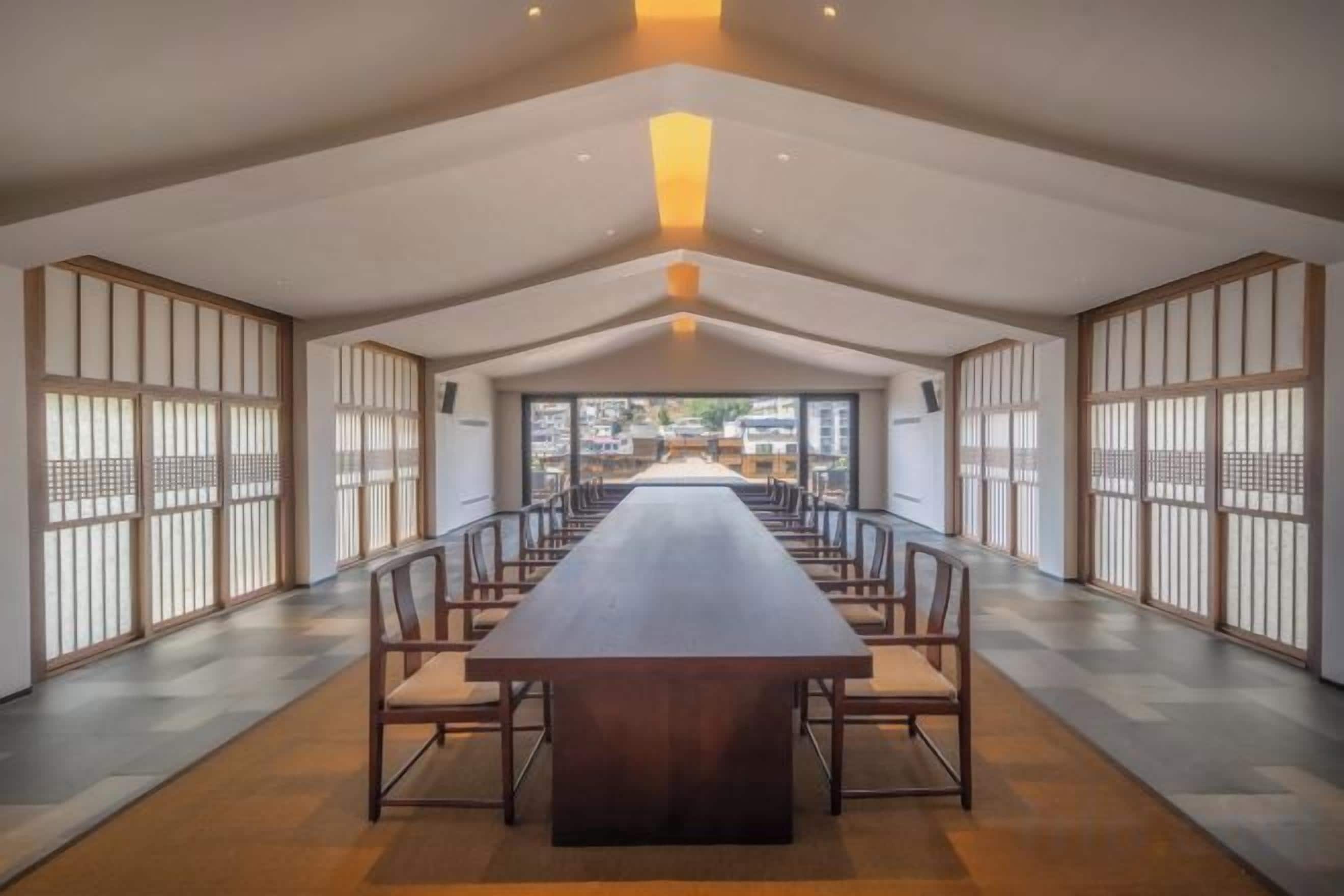 A long dining table with chairs, a high ceiling, and sliding doors on the sides.
