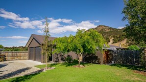 A residential backyard with a well-maintained lawn, a small tree, and a house with a sloped roof.