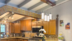 A modern kitchen with wooden cabinets, a central island with seating, and a stone accent wall. - ST.JOHN, VIRGIN ISLANDS!  2 BEDROOM, 1.5 BATH, BEAUTIFUL TROPICAL GARDENS! (St. John)