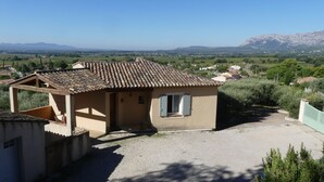 A small, single-story building with a tiled roof, a balcony, and a gravel driveway. - L'Olivette (Pourrières)