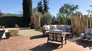 A wooden deck with outdoor furniture, a koi pond, and a backdrop of trees and mountains. - L'Olivette (Pourrières)