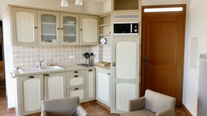 A compact kitchen with white cabinets, a sink, a microwave, and a clock on the wall. - L'Olivette (Pourrières)