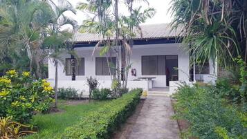 A white building with a tiled roof, surrounded by lush greenery and palm trees.