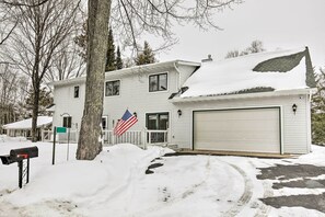 Uma casa de dois andares com garagem, rodeada por terreno e árvores cobertas de neve.