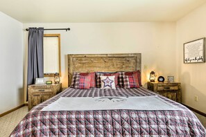 Quarto com colcha xadrez, cabeceira de madeira e um letreiro fixado na parede.