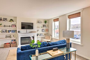 Een woonkamer met een blauwe bank, een glazen salontafel, een open haard en een aan de muur bevestigde televisie.