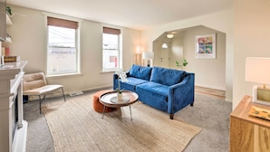 A living room with a blue sofa, a round coffee table, a beige armchair, and a small orange ottoman. - Cincinnati Vacation Rental: 6 Mi to Downtown! (Cincinnati)