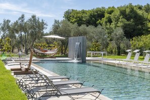 Relax by the serene pool surrounded by lush greenery and trees, complete with lounge chairs and a hammock.
