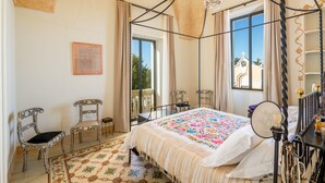 A bedroom with a four-poster bed, a chandelier, a balcony with a view of a church, and two ornate chairs. - CASIN ANAND (Novoli)