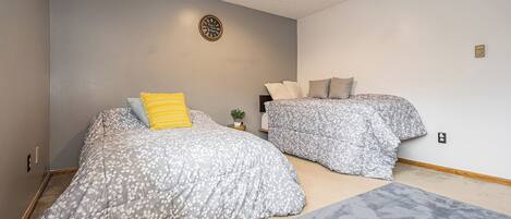 A bedroom with two beds, a ceiling fan, a wall clock, and a small plant.